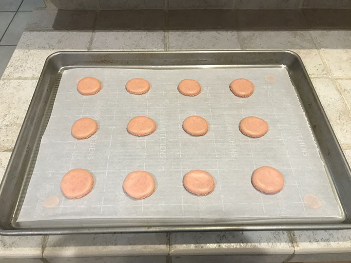 Baked pink macaron shells on baking sheet